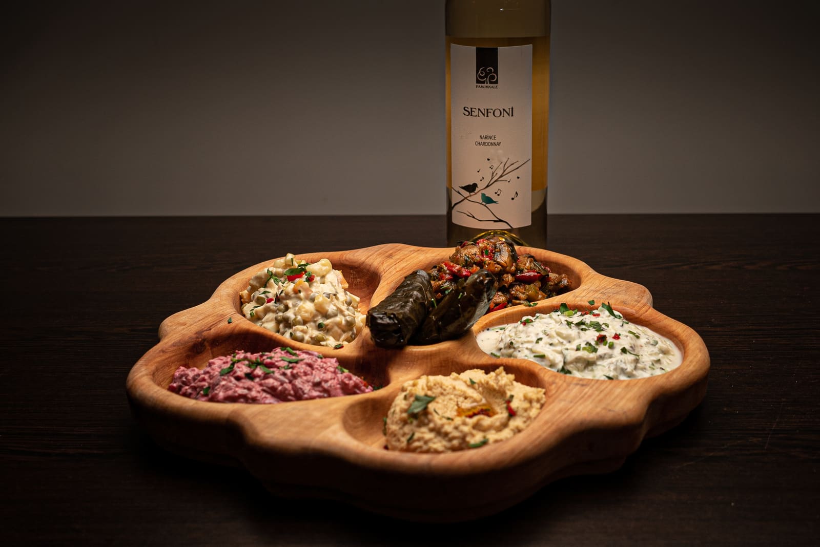A wooden platter of cold mezze — hummus, cacık, a beetroot dip, smoked aubergine and a stuffed vine leaf