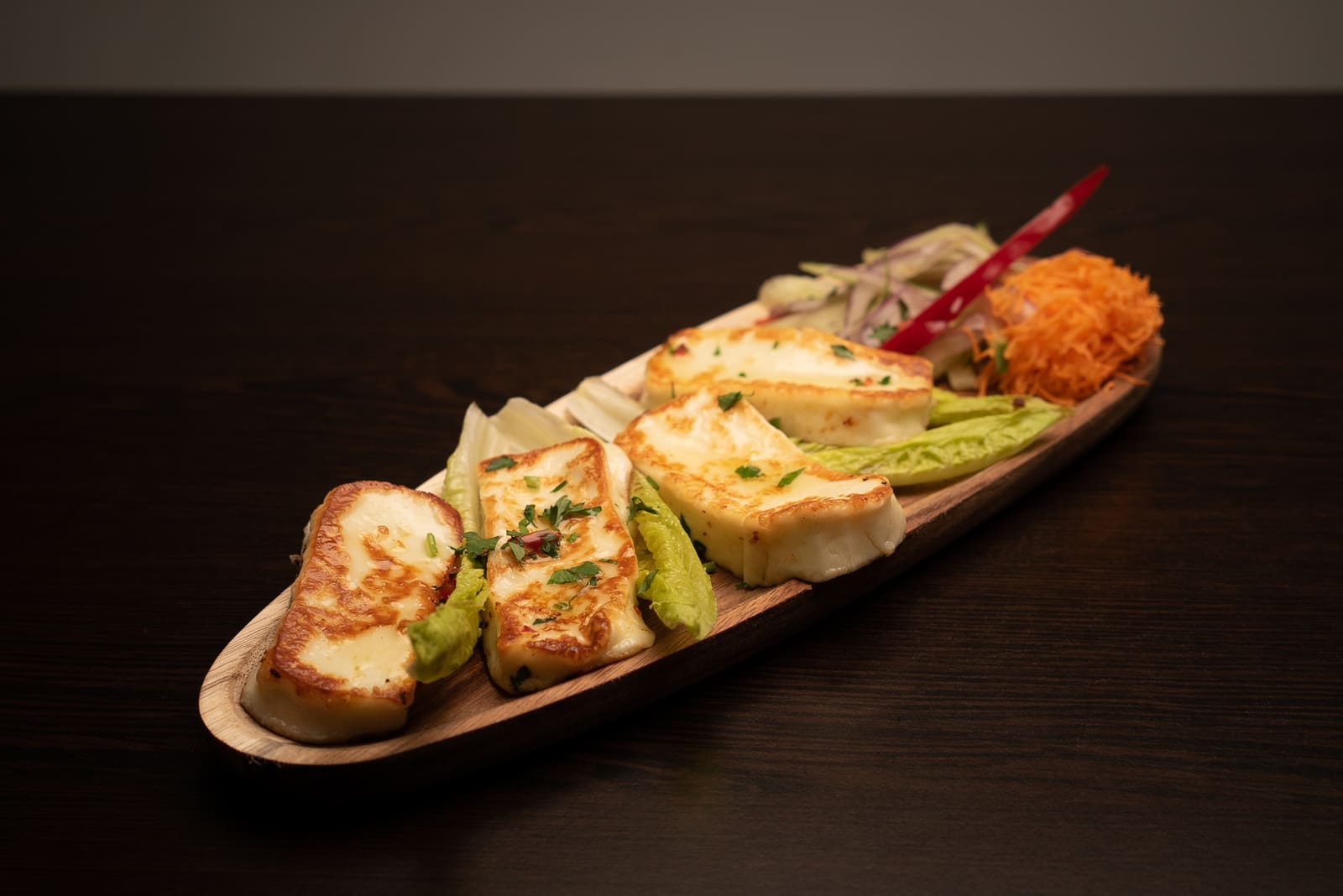 Grilled halloumi on a long wooden board with salad leaves