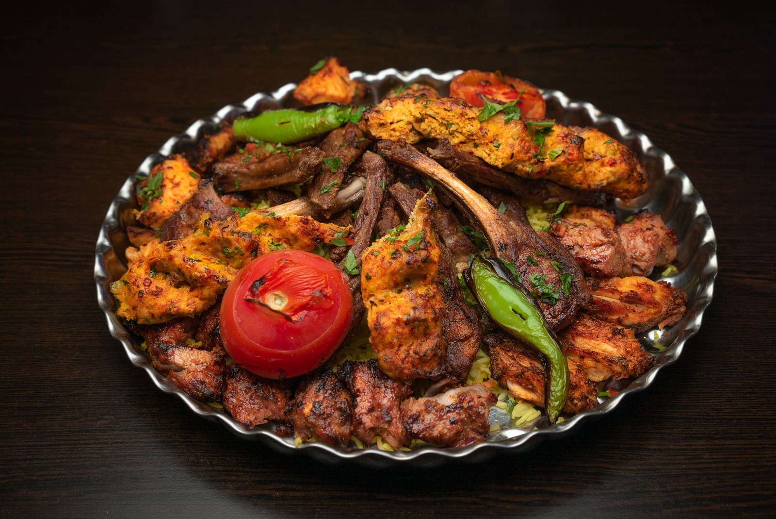 Lamb chops, chicken and kofte piled on a silver platter with grilled peppers and tomato