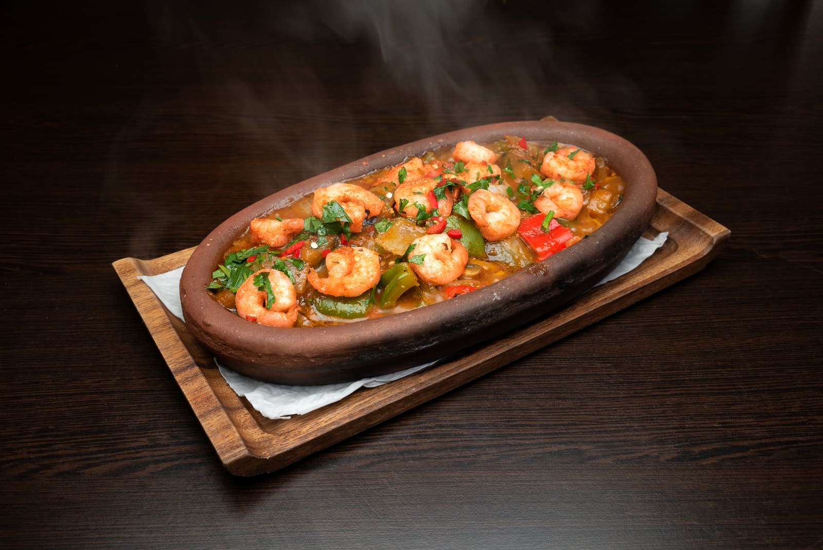 Prawns with peppers in a clay dish, still steaming as it reaches the table