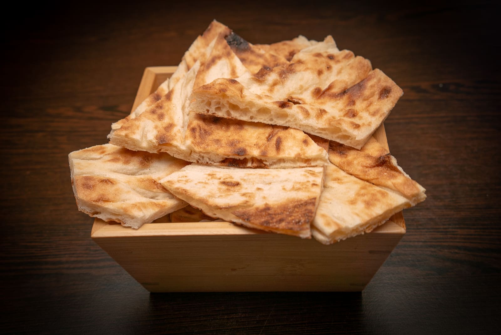 Blistered Turkish flatbread torn into pieces and piled in a wooden bowl