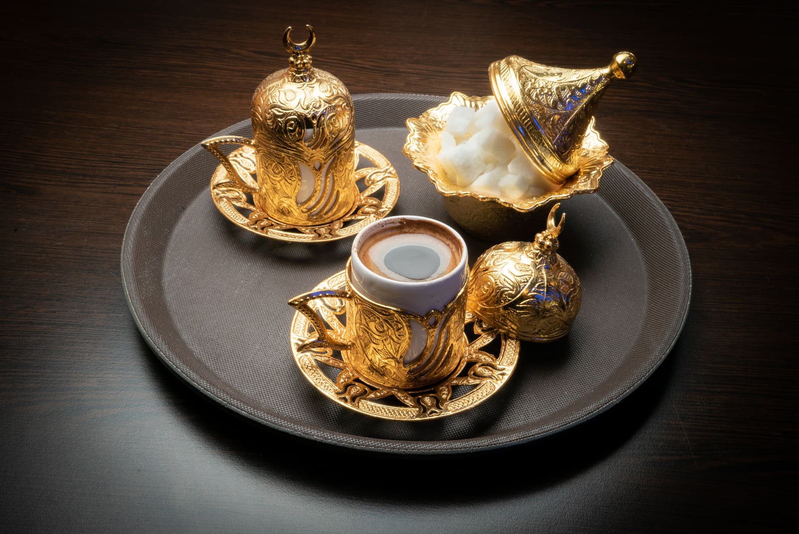 Turkish coffee served in an engraved gold cup with a bowl of Turkish delight beside it