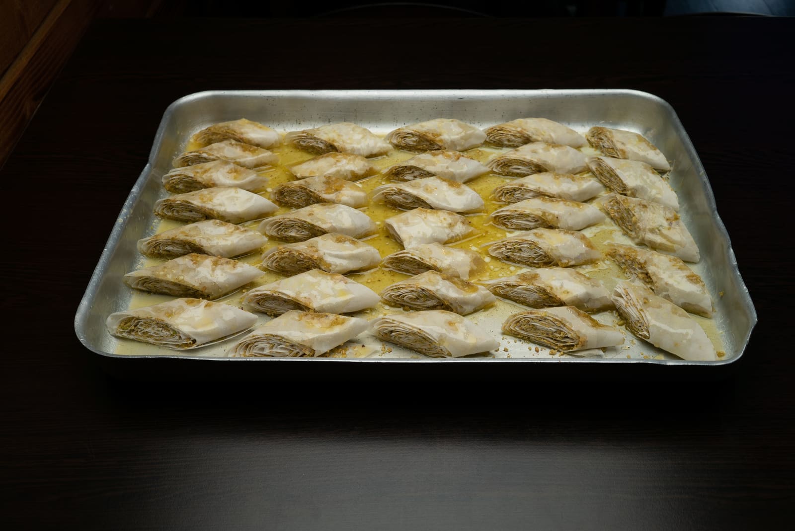 A full tray of vine leaves rolled by hand before service, glossy with olive oil